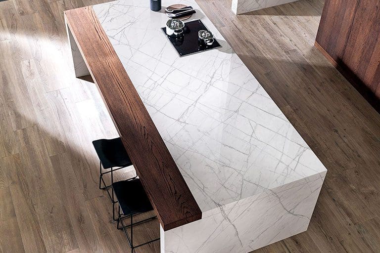 Modern kitchen island with a natural stone countertop and wooden side panel, including black stools on a wooden floor.