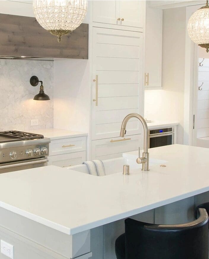 Modern kitchen interior featuring white cabinetry, marble backsplash from a countertop company, and an island with a sink under hanging pendant lights.