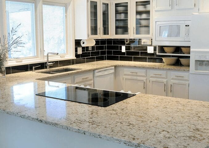 Modern kitchen interior with white cabinets, black backsplash, granite countertops from a top countertop company, and built-in appliances.