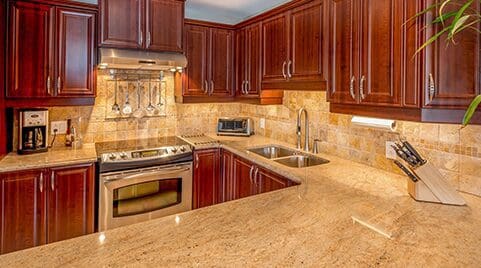 Modern kitchen with dark wood cabinets, stainless steel appliances, and a tan tiled backsplash by a leading countertop company.