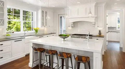 Bright, modern kitchen featuring white cabinetry from a leading countertop company, an island with bar stools, pendant lights, and hardwood floors.