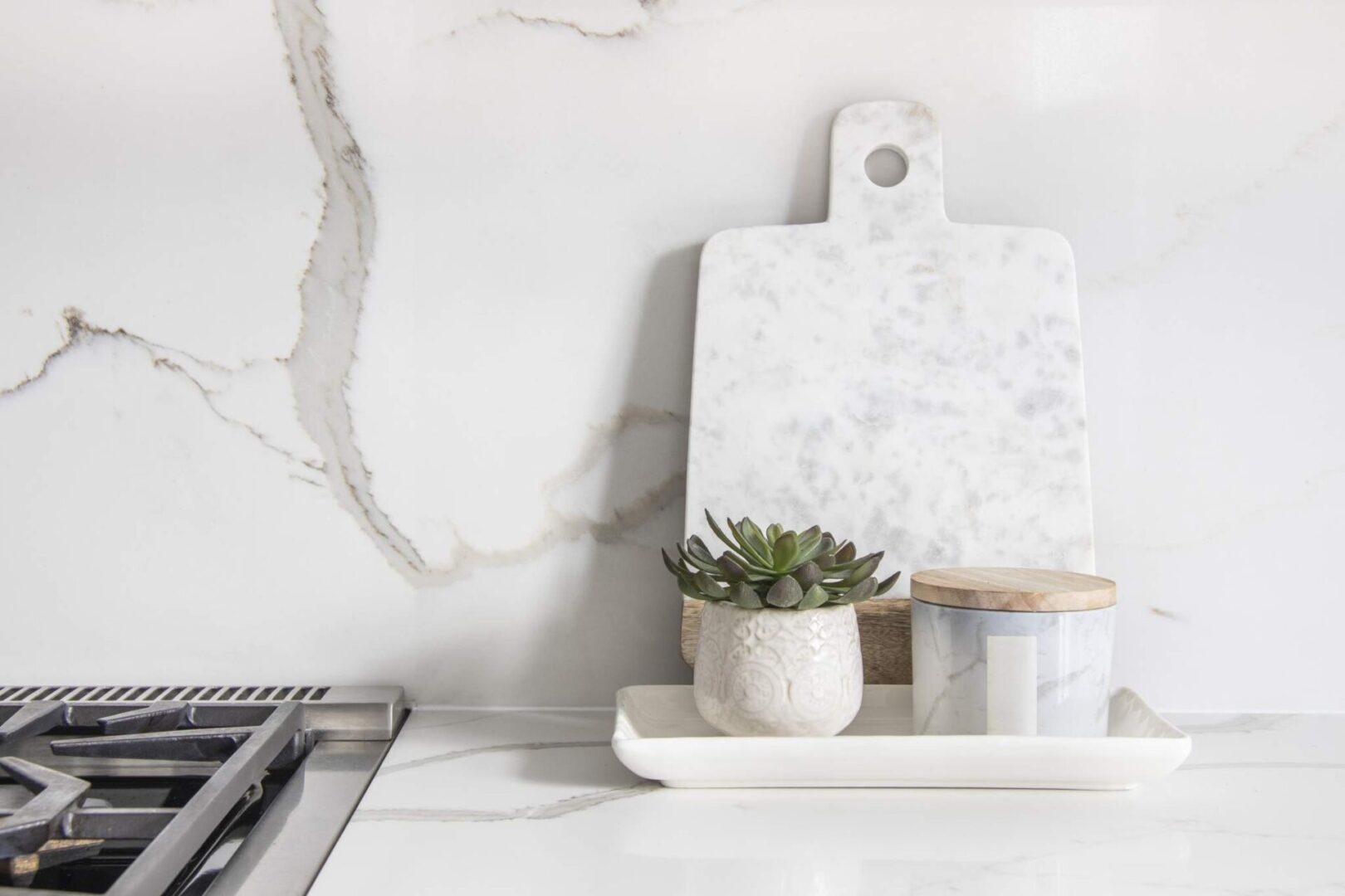 A marble cutting board beside a succulent plant and a marble container on countertop remnants near a stove.