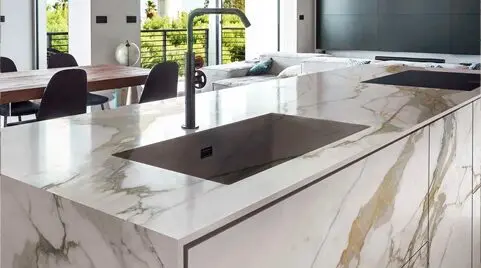 A modern kitchen with marble countertops, an undermount sink, and a view of the dining area through sliding glass doors.