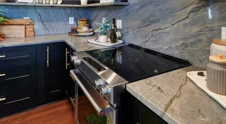 Modern kitchen installed by a countertop company with black cabinetry, stainless steel appliances, and grey marble countertops and backsplash.