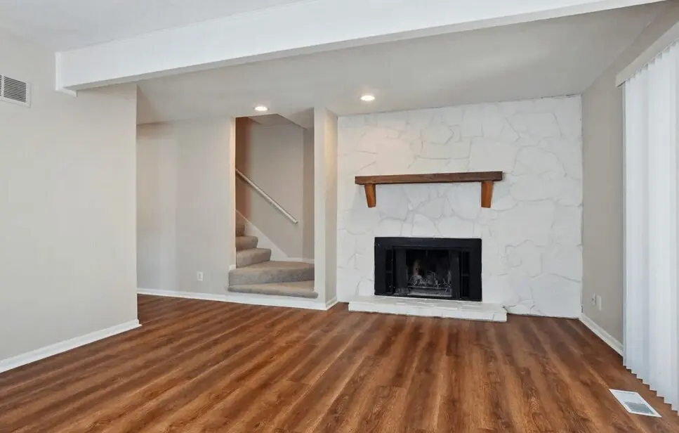 Interior of a modern living room with hardwood floors, a white fireplace, and stairs leading to another level.