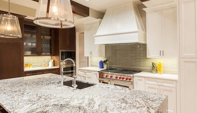 Modern kitchen with white cabinetry, marble countertops, and a red stove, under warm lighting.