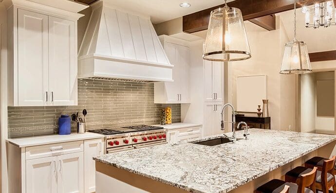 Modern kitchen interior featuring white cabinets, marble countertops, and pendant lighting over an island.