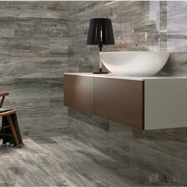 Modern bathroom with gray stone tile walls and carpet flooring, featuring a wooden vanity with a white basin and a black lamp.