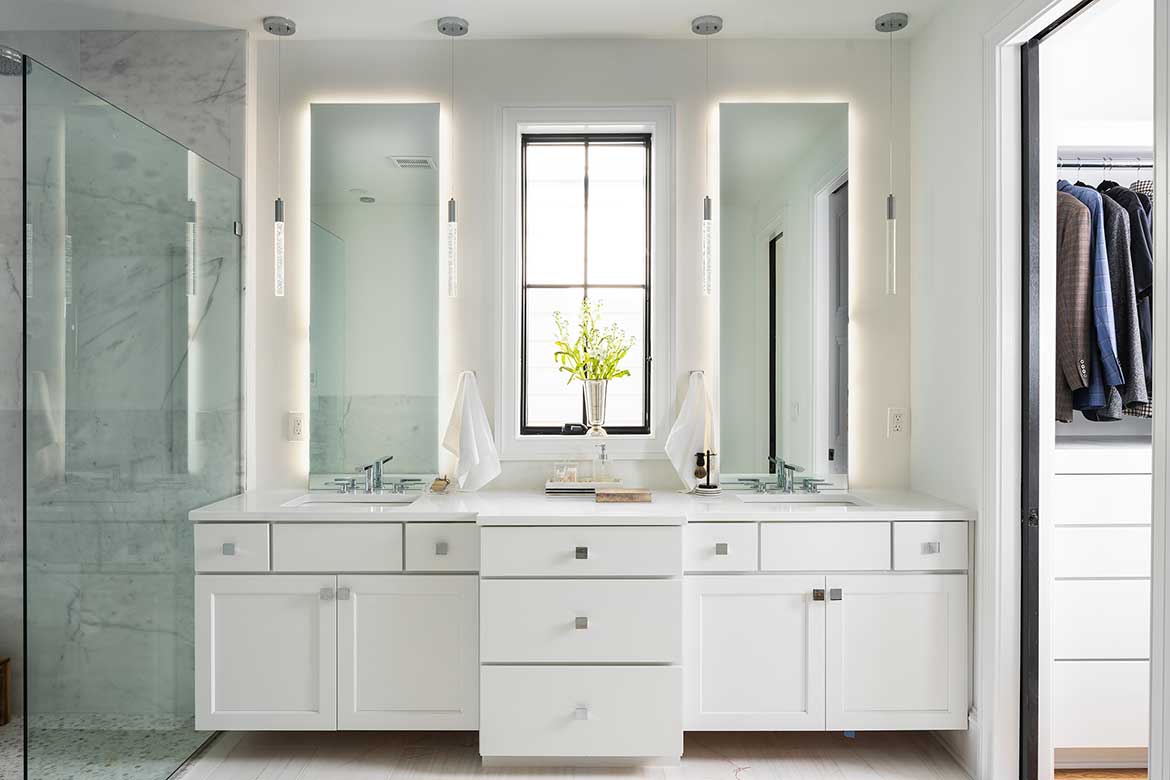 Modern bathroom with double vanity, mirrors, and a small window above the sink reflecting a marble shower and adjacent flooring projects.