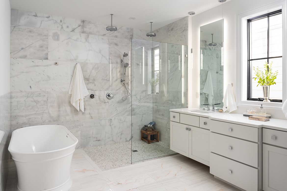 Modern bathroom with white marble flooring projects and walls, featuring a freestanding bathtub, glass shower, and dual-sink vanity.