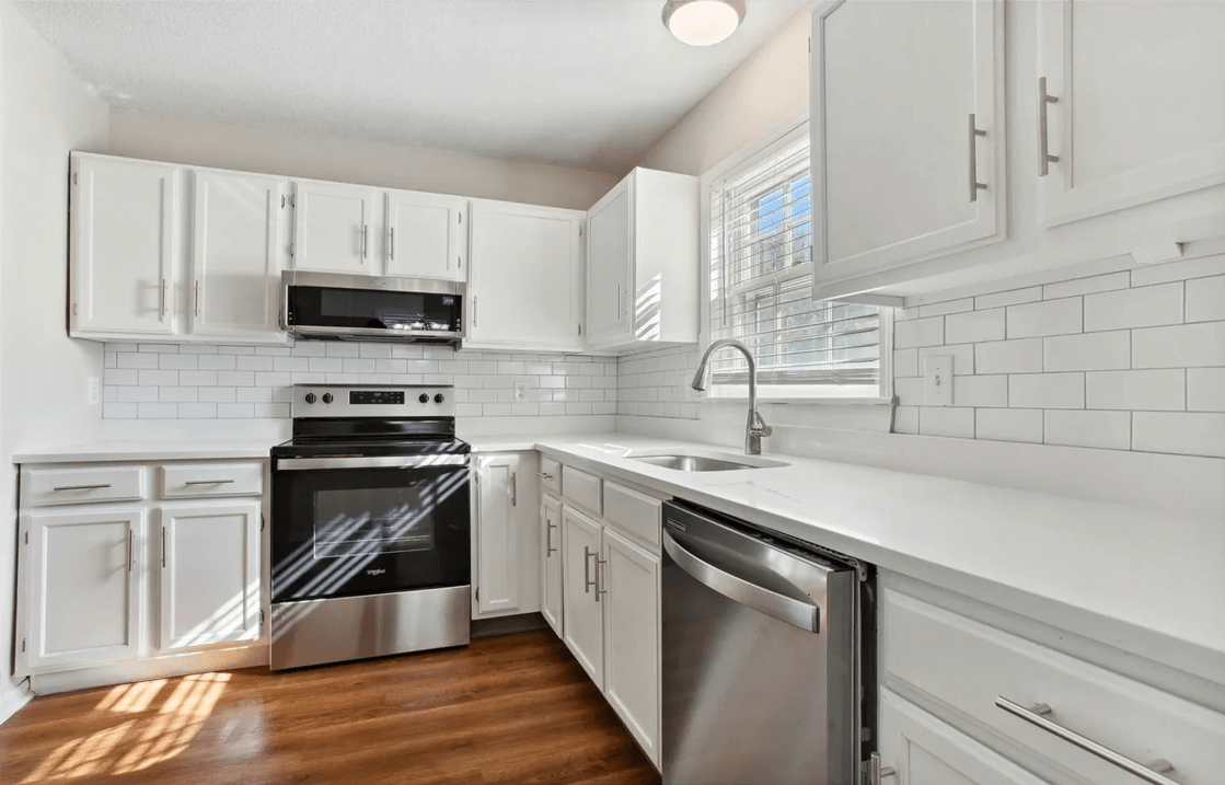 Modern kitchen interior with white cabinetry, stainless steel appliances, and hardwood floors illuminated by natural light from countertop company.