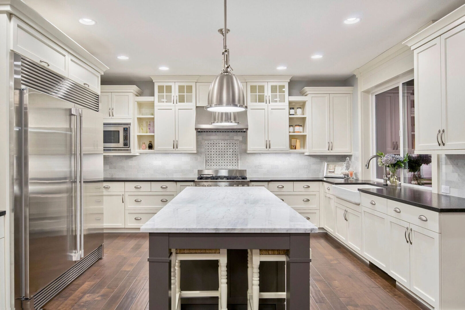 Modern kitchen with white cabinetry, stainless steel appliances, a large island with a quartz countertop, and pendant lighting.