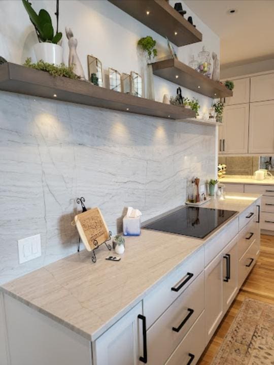 Modern kitchen interior with white cabinetry, marble countertops, and wooden floating shelves adorned with plants and Any Top Shop prices decor.