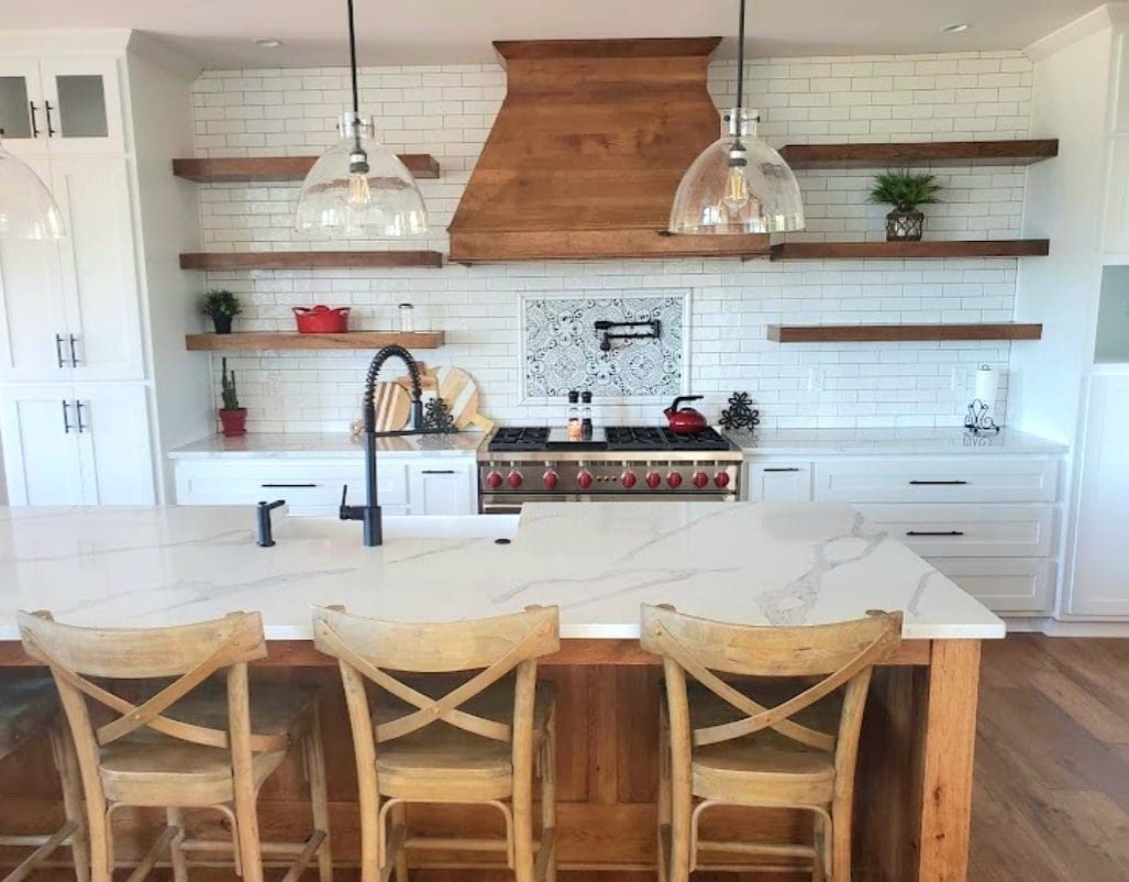 A modern kitchen with white subway tiles, wooden accents, two pendant lights, and a marble island with wooden stools, showcasing recent flooring projects.