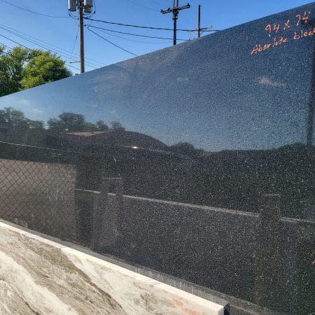 Reflective sound barrier beside a road with trees and power lines in the background, graffiti and countertop remnants on its surface.