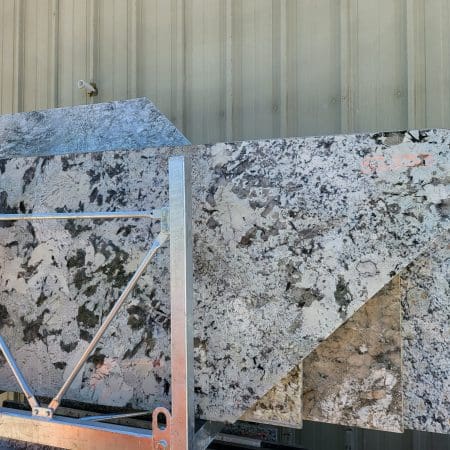 Two large granite countertop remnants leaning against a metal rack outside a building with a corrugated metal wall.