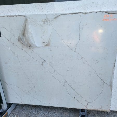 Large slab of white marble countertop remnants with gray veining, featuring a prominent crack and a damaged corner, stored upright outside.