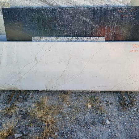 Stacked countertop remnants in various colors and textures, leaning against a wall outdoors.