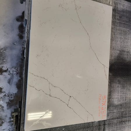 A sample of marble-like ceramic tile with delicate grey veining, displayed on a countertop remnants fabric surface.