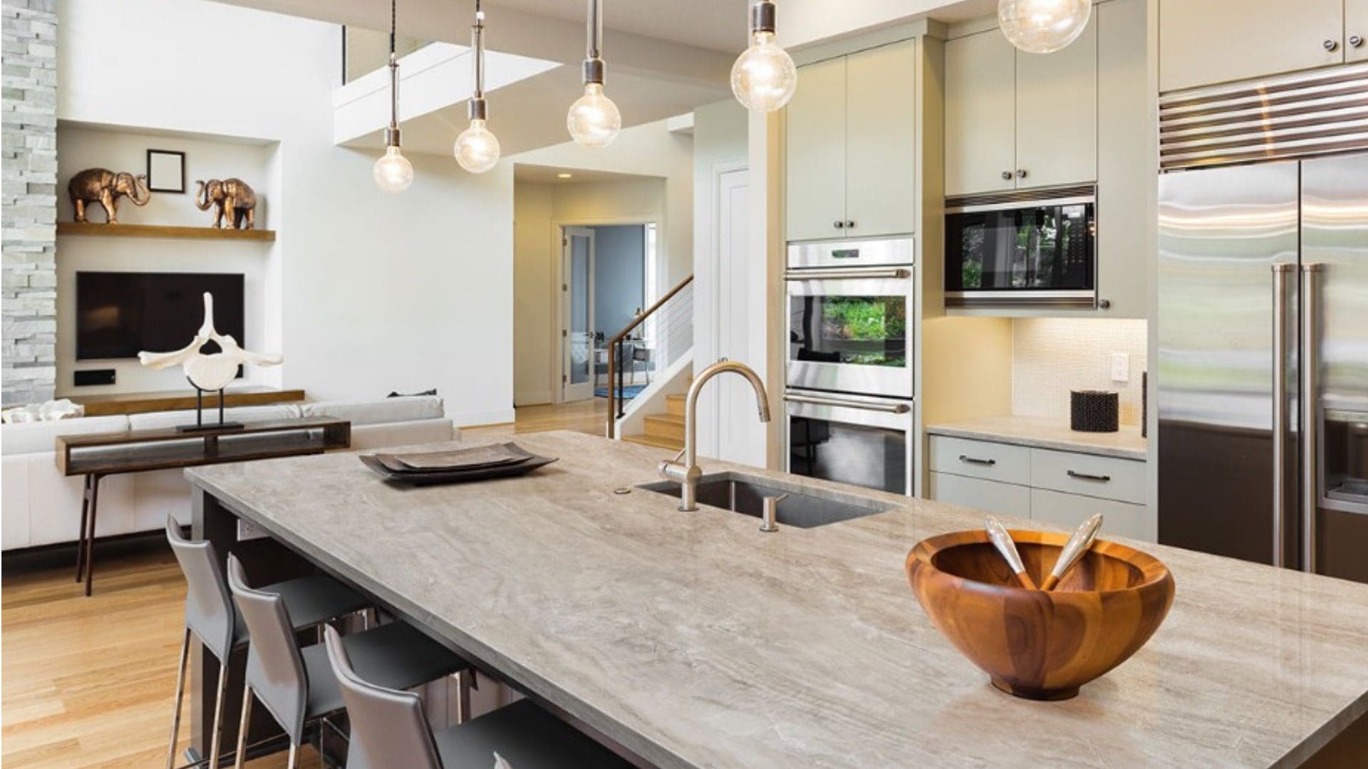 Modern kitchen with large island, hanging pendant lights, and stainless steel appliances, featuring a minimalist decor style with porcelain slab installation.