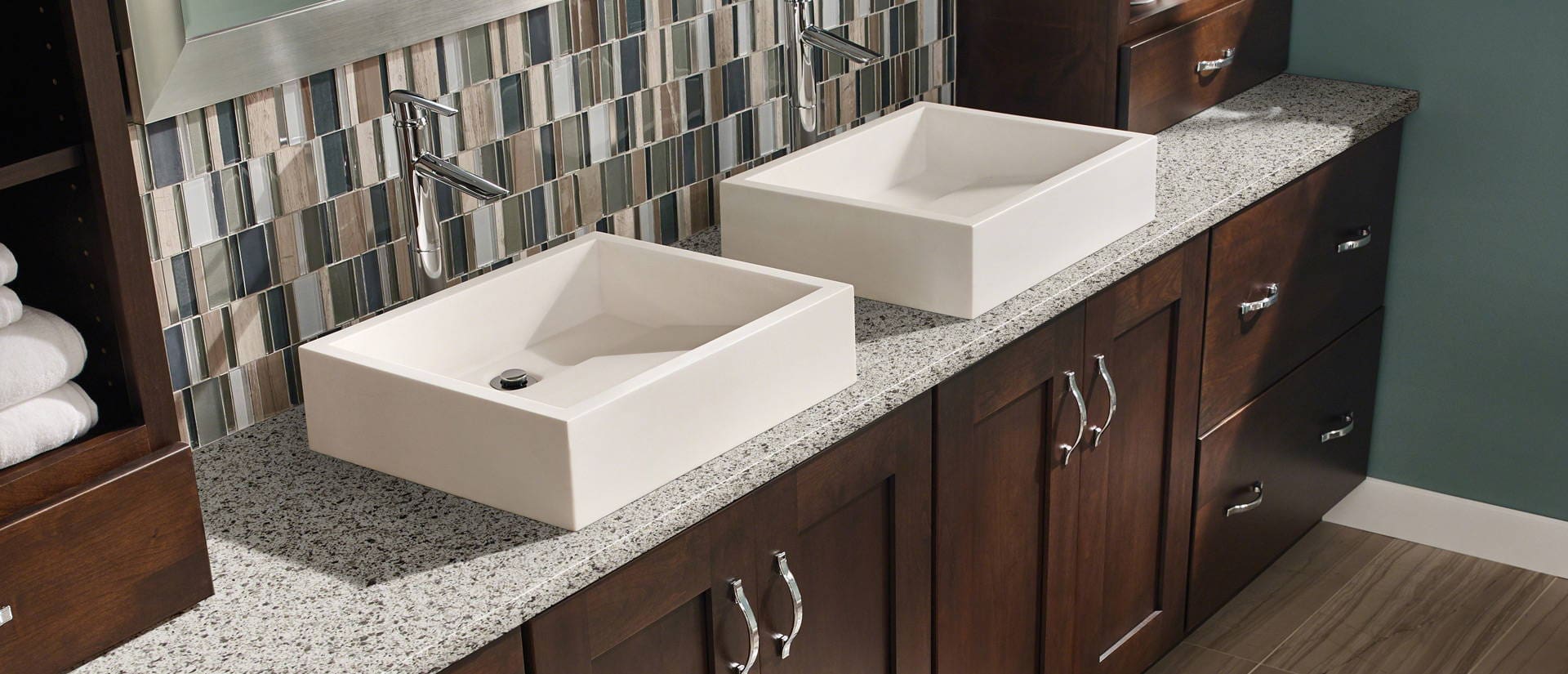 Two Any Top Shop square vessel sinks on a speckled countertop with dark wood cabinets and a mosaic tile backsplash.