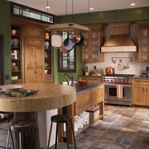 A rustic kitchen with wooden cabinets, custom countertops, a central island with bar stools, hanging pots, and a red stove.