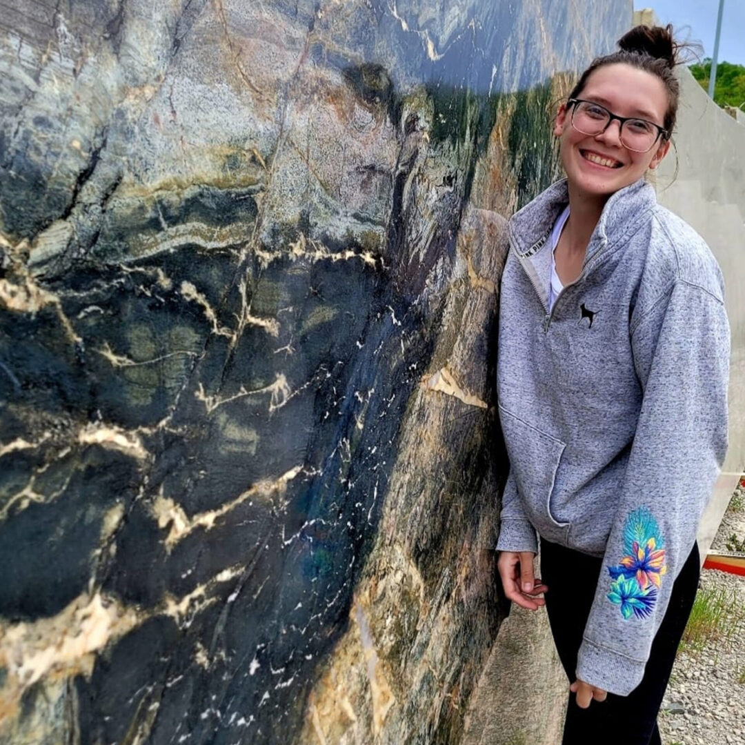 Hope from Any Top Shop standing beside a dramatic natural stone slab in the countertop showroom.