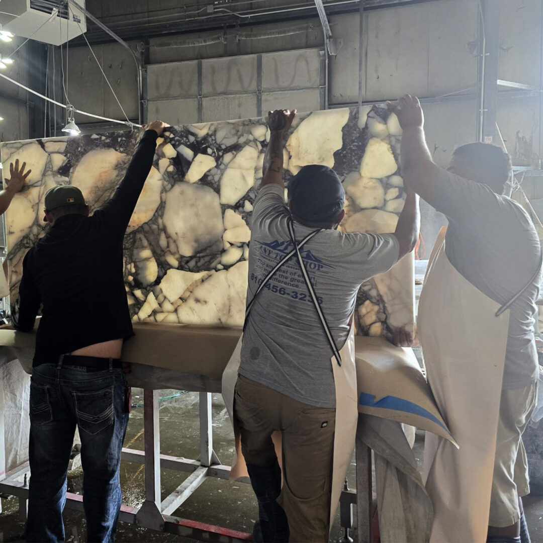 Three countertop installers positioning a backlit natural stone (marble) slab during fabrication at Any Top Shop in Kansas City.