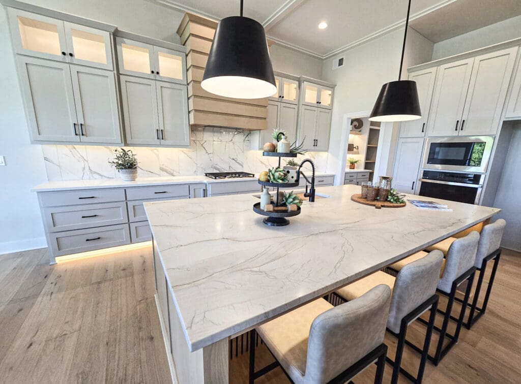 Luxury kitchen featuring a large quartzite waterfall island, full-height quartzite backsplash, custom gray cabinetry, pendant lighting, and premium modern finishes.