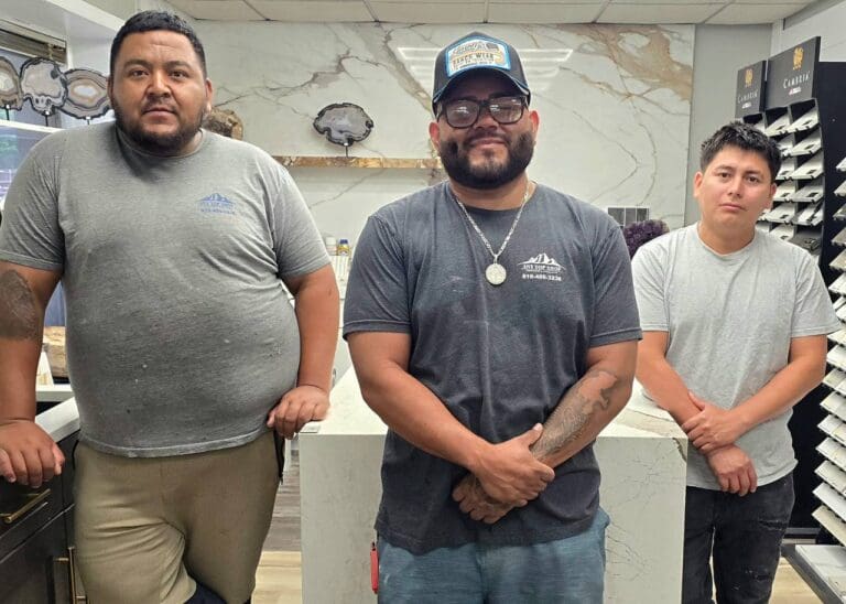 Dave, Oliver, and Ferdin of the AnyTopShop fabrication team standing in the countertop showroom surrounded by premium stone slab samples and custom countertop displays in the Kansas City metro area.
