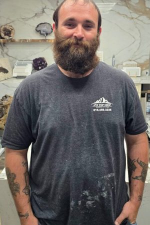 Austin, professional installer at Any Top Shop, standing in front of a natural stone slab in the countertop showroom